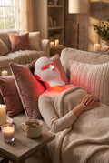 Woman relaxing on a sofa wearing the Hushvale LED light therapy mask with a cup of tea
